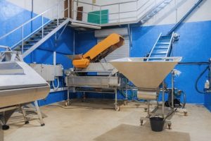 Industrilokal med maskiner, transportband och trappor i en verkstadsmiljö.